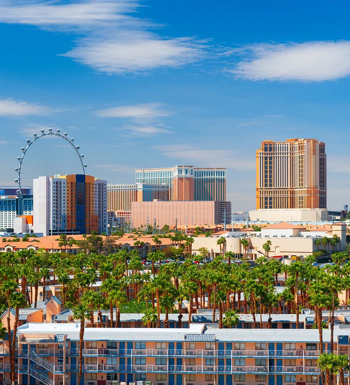 A vibrant Las Vegas skyline featuring modern hotels, palm trees, and the High Roller observation wheel under a clear blue sky.