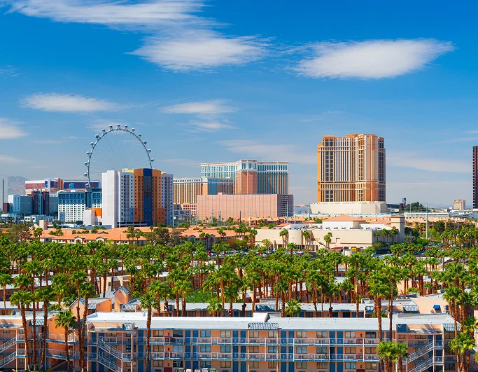 Skyline of Las Vegas with the High Roller Ferris wheel, palm trees, and multiple hotels under a blue sky.